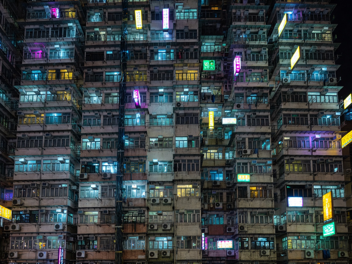 A dense residential tower at night, every balcony crowded with air-conditioning units and hanging cables, illuminated signs in several scripts stacked up the facade
